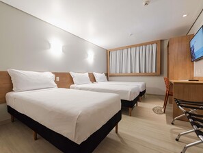 Une chambre d’hôtel avec deux lits, un bureau, une chaise, une télévision et une fenêtre avec des rideaux.