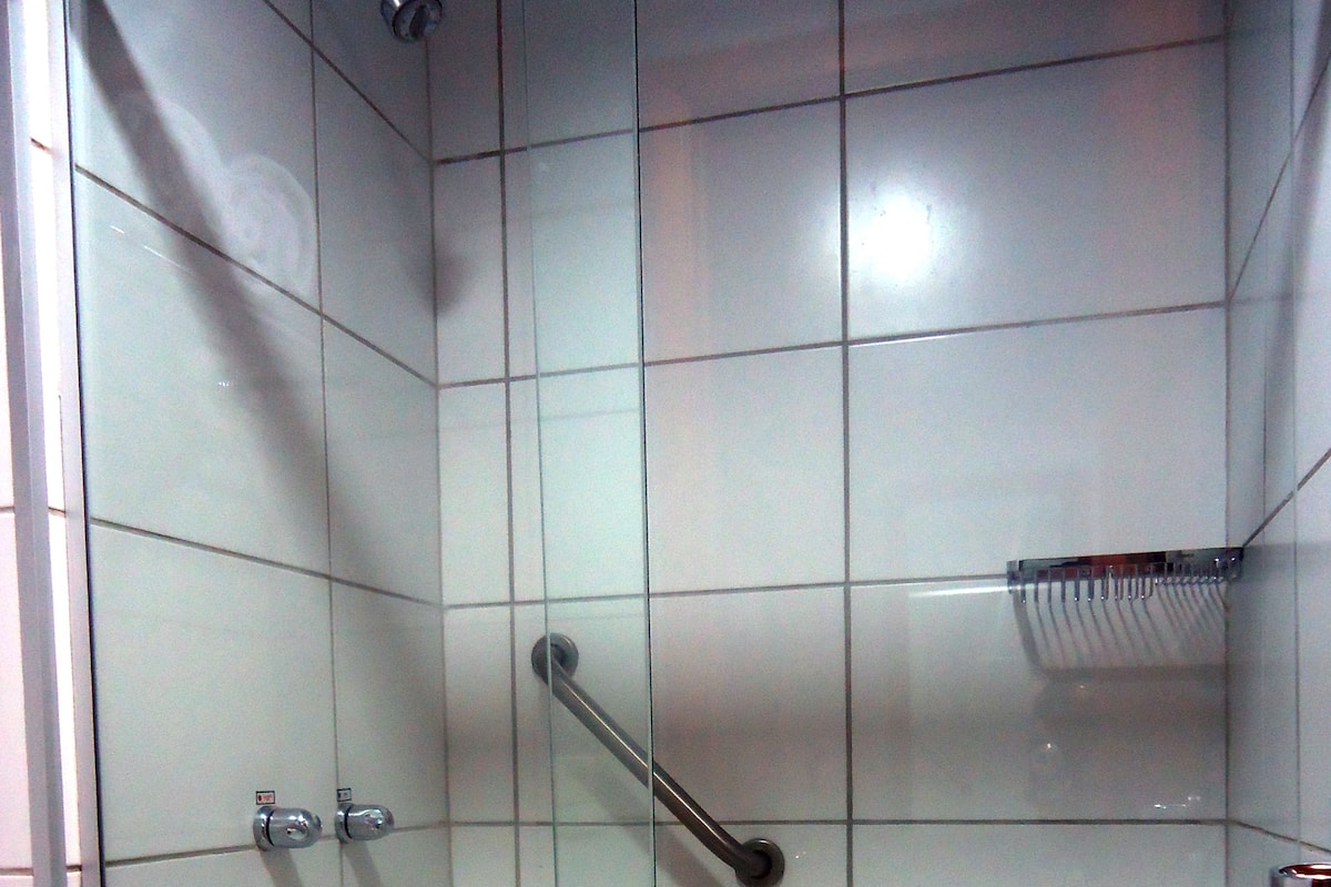 A tiled shower stall with a glass door, a handrail, and a showerhead.