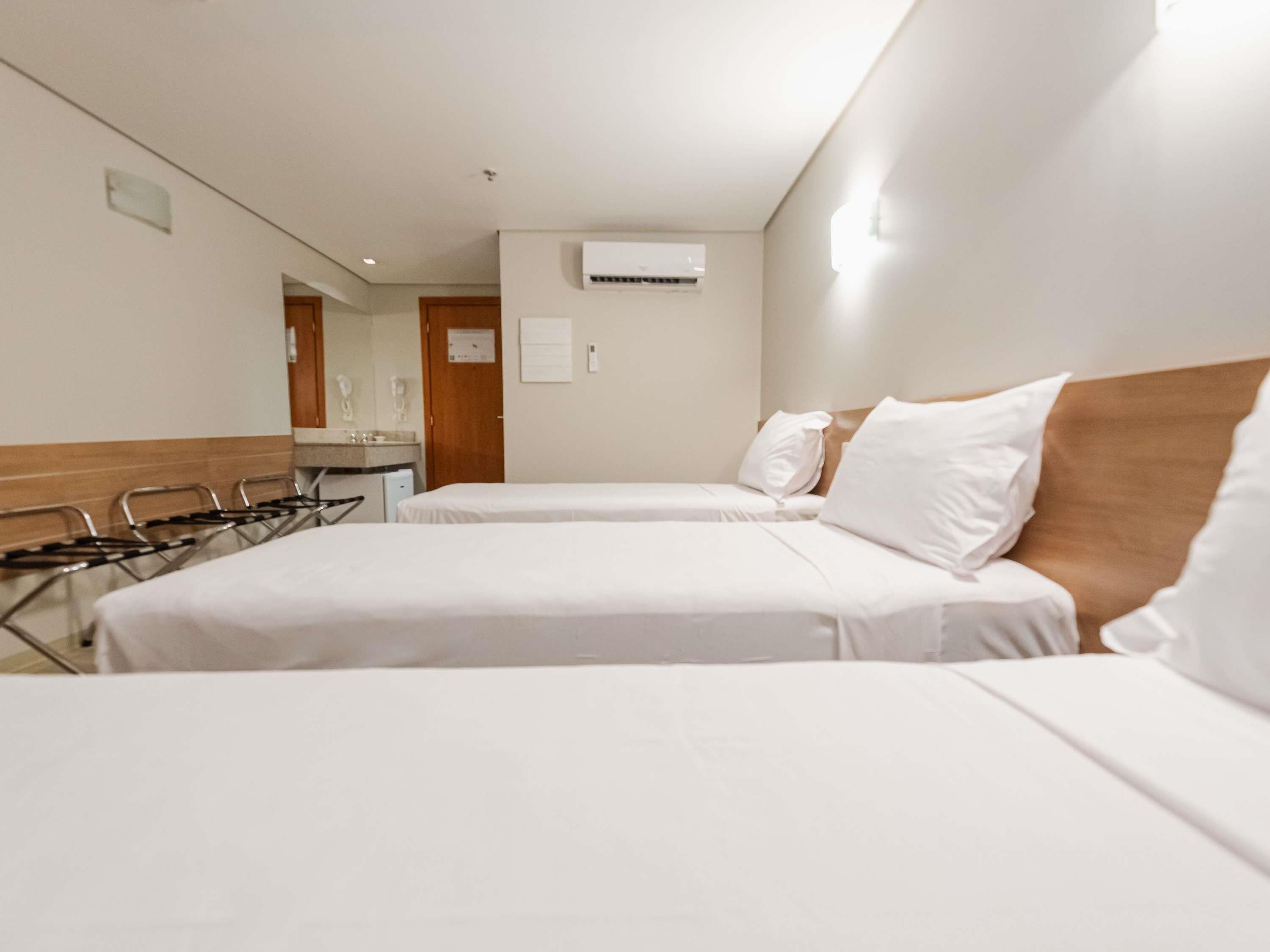 A hotel room with two beds, a mirror, a sink, and an air conditioning unit.