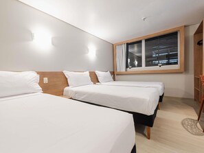 Een hotelkamer met twee bedden, een raam met zonwering, een houten hoofdeinde en een lichtschakelaar aan de muur.