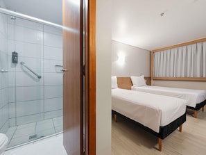 Une chambre dâhĂŽtel avec une douche, deux lits, une tĂȘte de lit en bois et un luminaire.