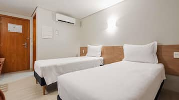 Habitación de hotel con dos camas individuales, una puerta de madera, un equipo de aire acondicionado y un interruptor de luz en la pared.