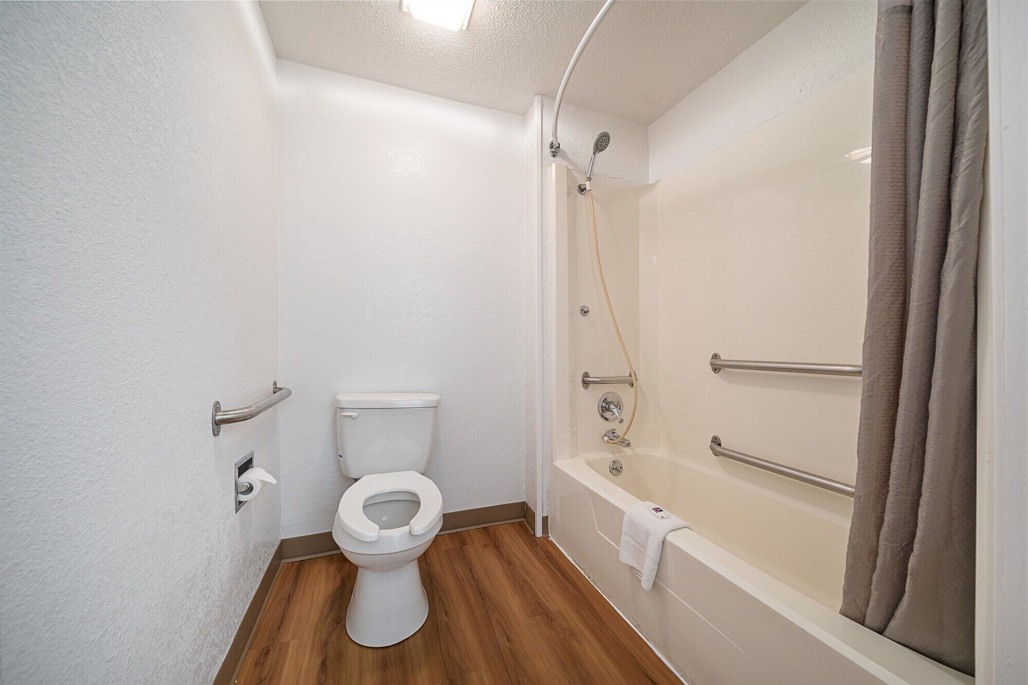 A bathroom with a toilet, a shower with a grab bar, and a bathtub.
