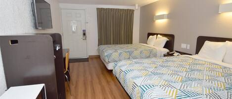 A hotel room with two beds, a desk, a chair, a television, and a door.