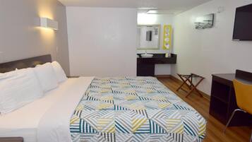 A hotel room with a bed, a desk, a chair, a mirror, and a sink.