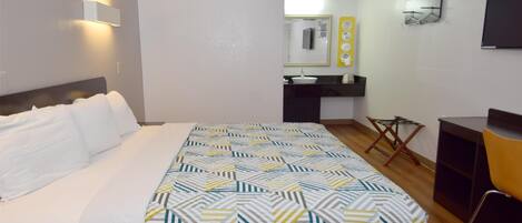 A hotel room with a bed, a desk, a chair, a mirror, and a sink.