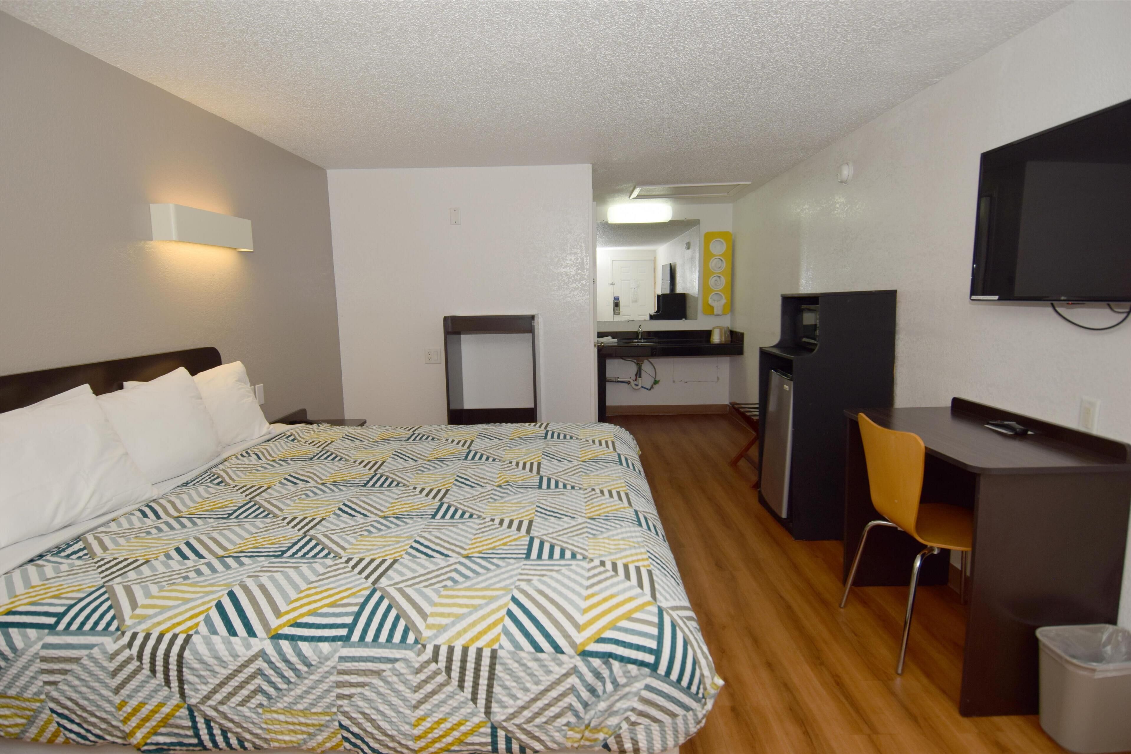 Une chambre d’hôtel équipée d’un lit, d’un bureau, d’une chaise, d’une télévision et d’une petite kitchenette.