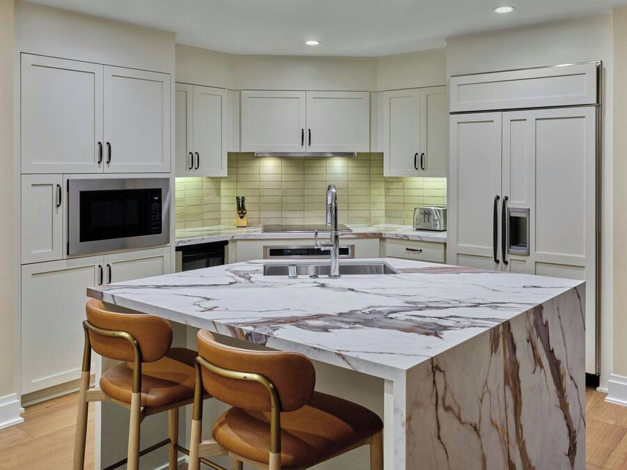 Una cocina moderna con armarios blancos, una isla de mármol y dos taburetes de bar.