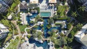 Vue aérienne d’un complexe hôtelier doté d’une piscine centrale, de plusieurs espaces de détente et d’une végétation luxuriante.
