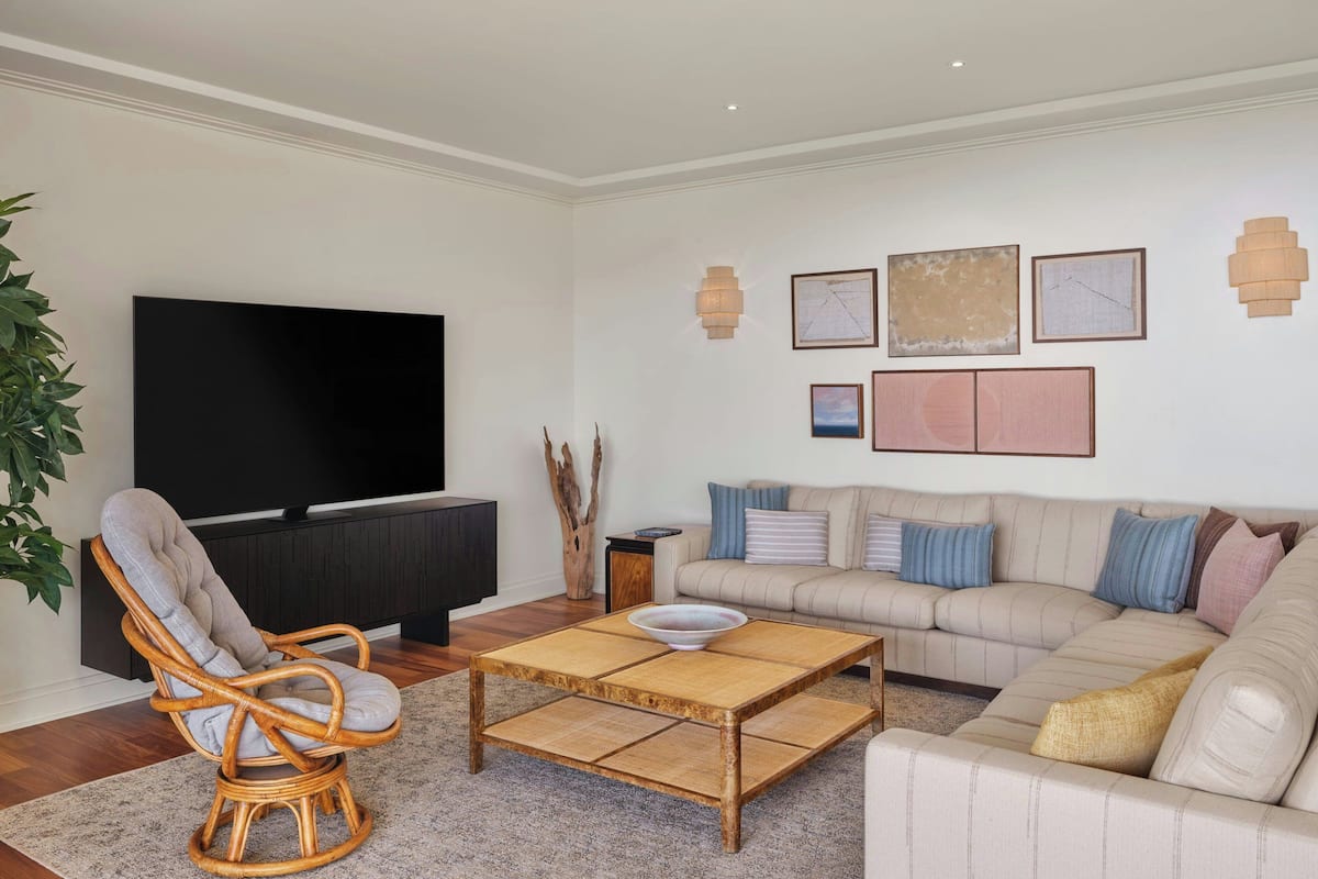 Een woonkamer met een televisie, een rieten stoel, een bank en een salontafel.