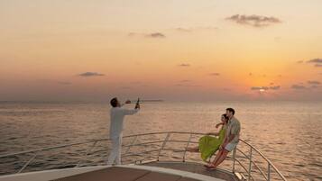 A boat with a metal railing, a person holding a bottle, and another person sitting on the deck.