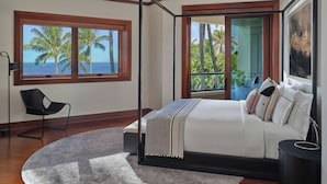 A bedroom with a four-poster bed, a view of the ocean, a chair, and a large window.