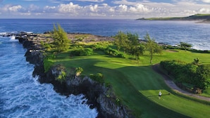 A coastal golf course with a view of the ocean, a clear sky, and a golfer on the green.