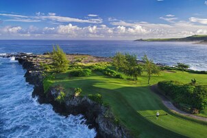 Un campo de golf costero con vistas al océano, cielo despejado y un golfista en el green.