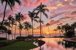 Vista del atardecer con palmeras y una piscina infinita.