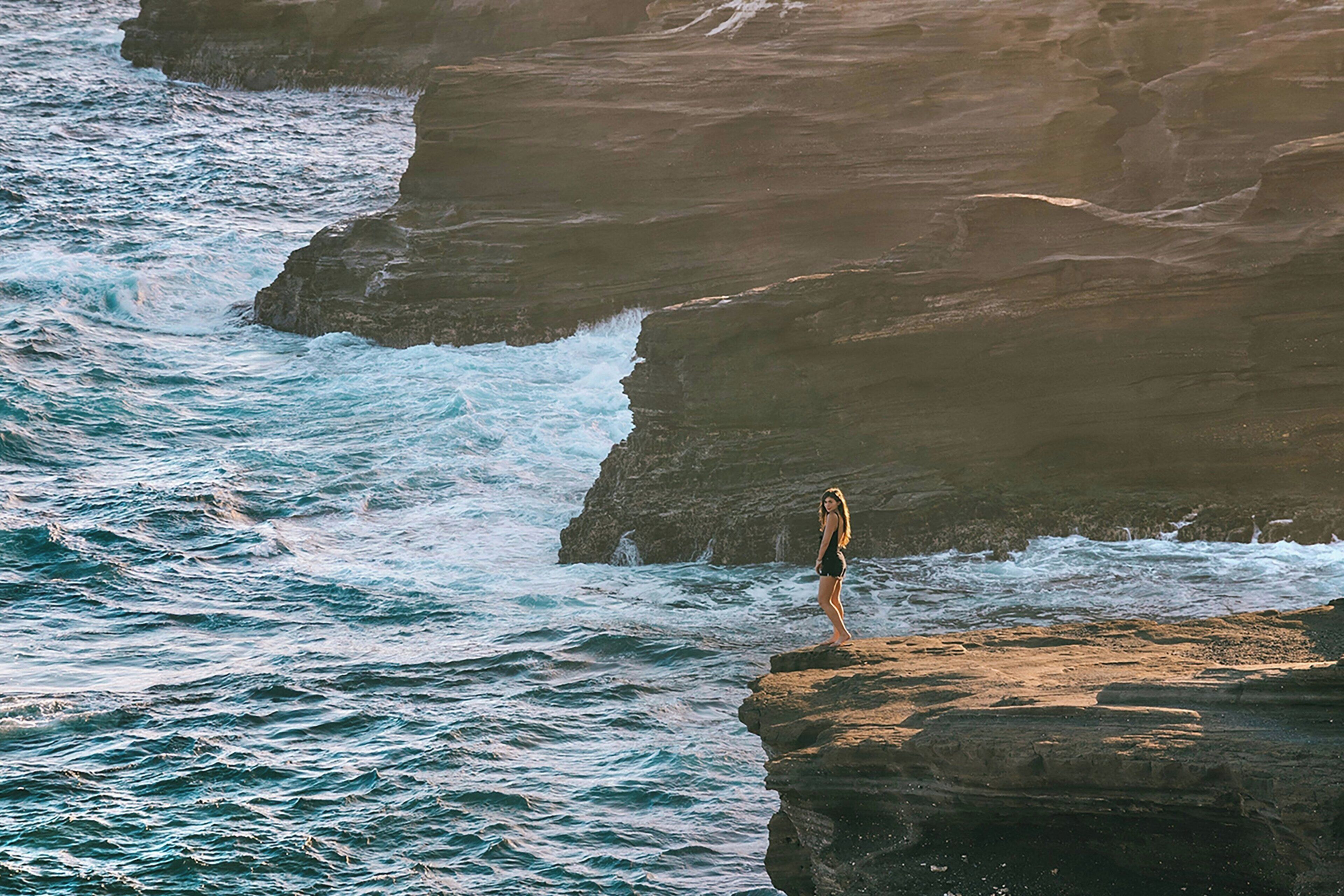 A person standing on a rocky outcrop by the sea.
