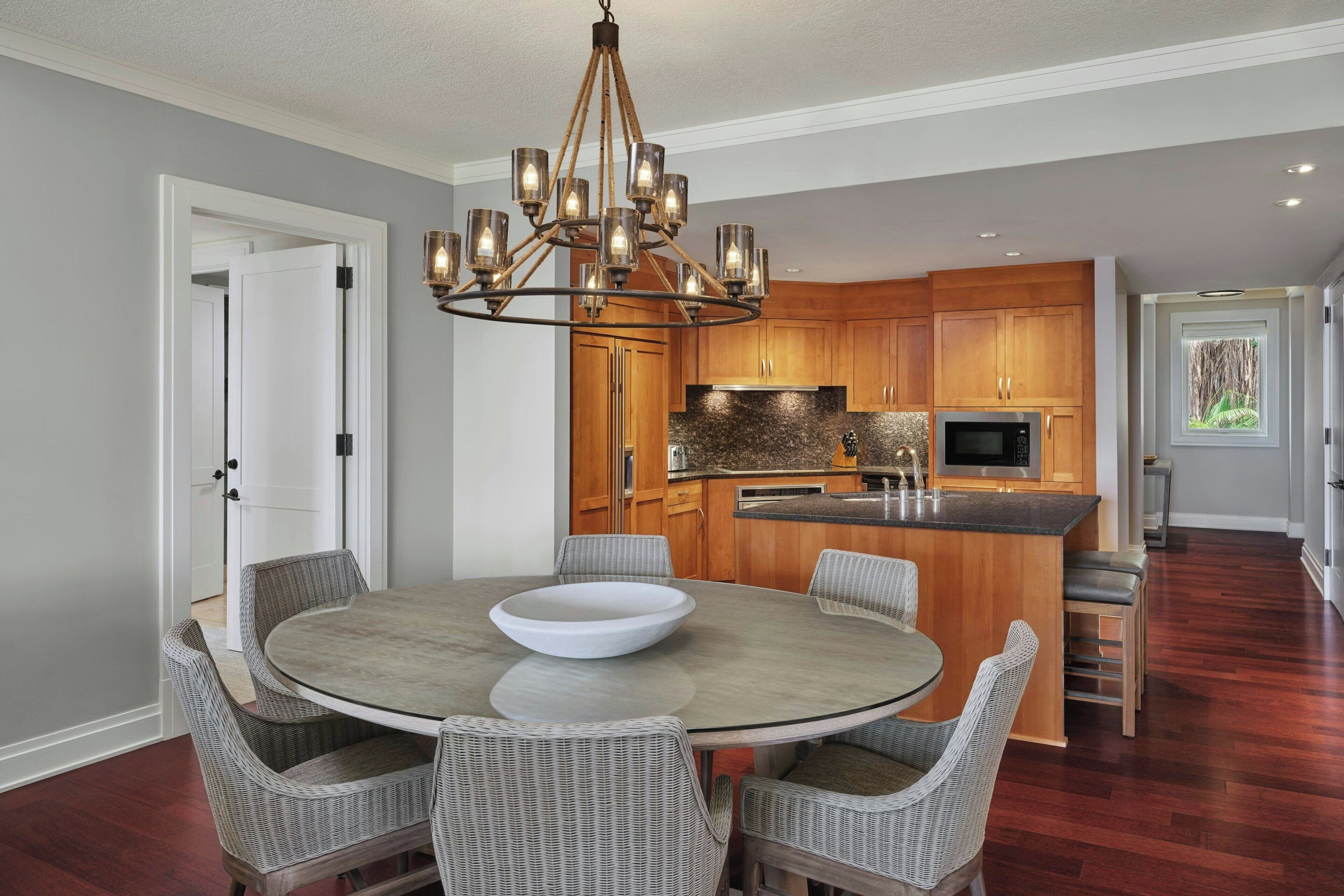 A modern kitchen with wooden cabinets, a built-in island, and a dining area with wicker chairs and a round table.