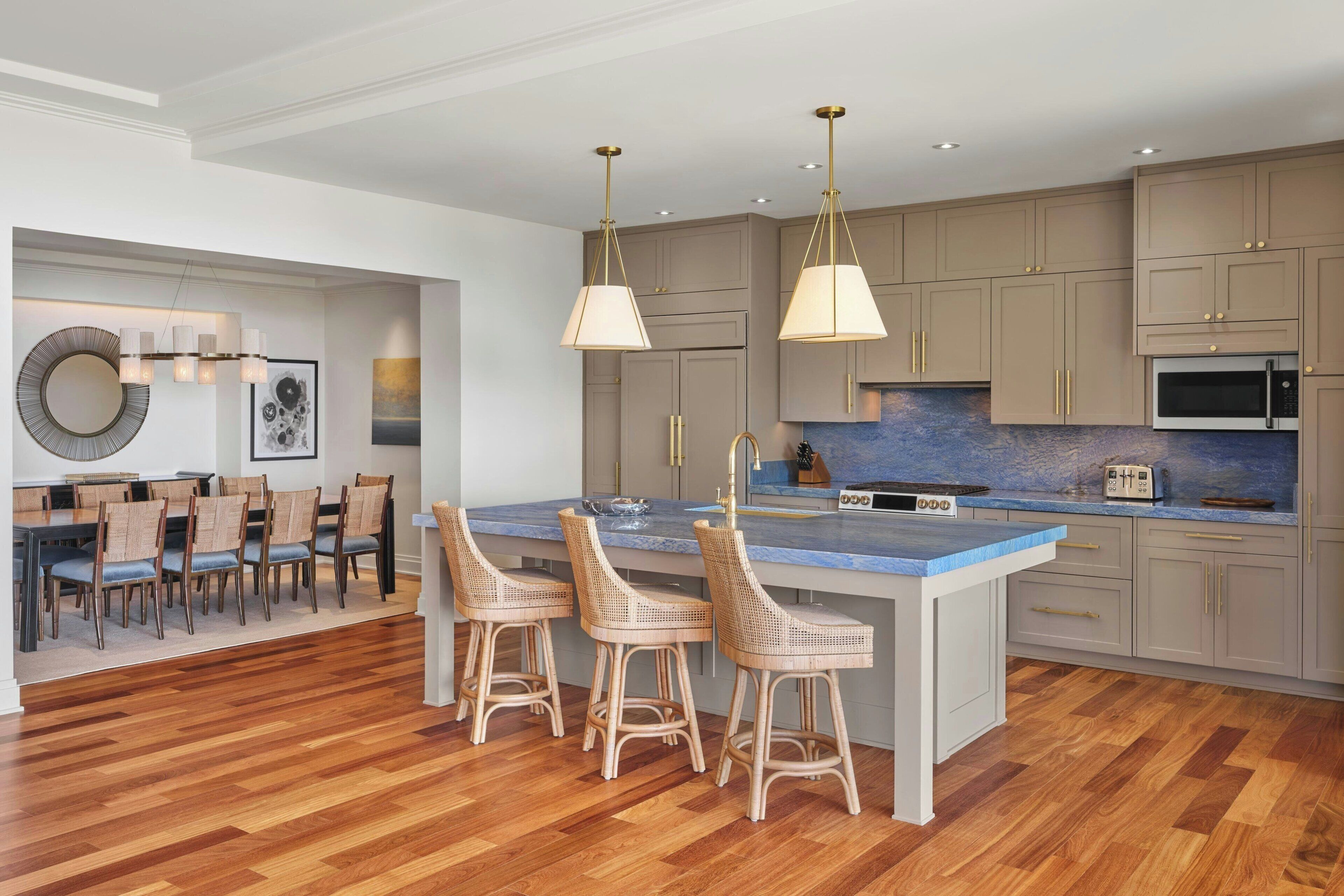 Una cocina moderna con una isla central, taburetes de bar, luces colgantes y un comedor con sillas y una mesa.