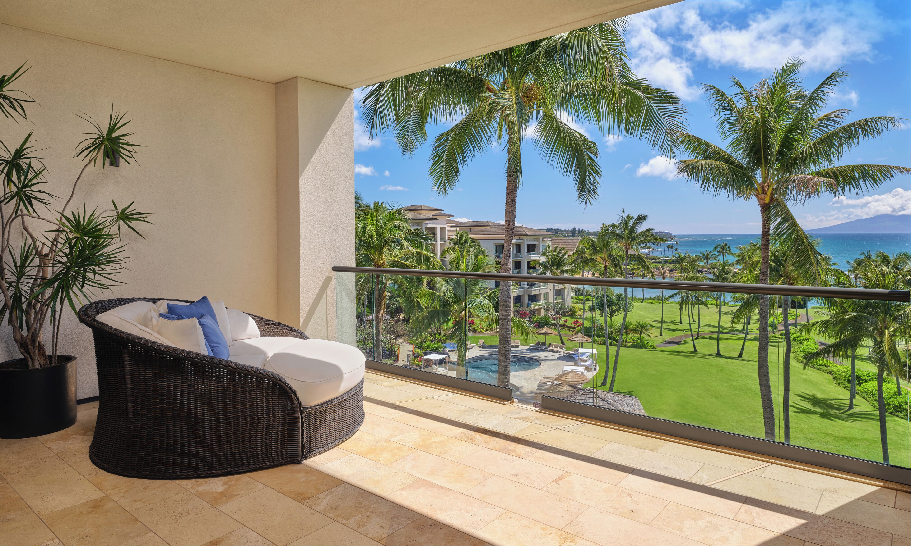 A balcony with a wicker chair, a potted plant, and a view of a golf course and ocean.