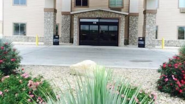 A building entrance with a stone facade, a large garage door, and a landscaped area with flowers and shrubs. - The Sagebrush Hotel (Crystal City)