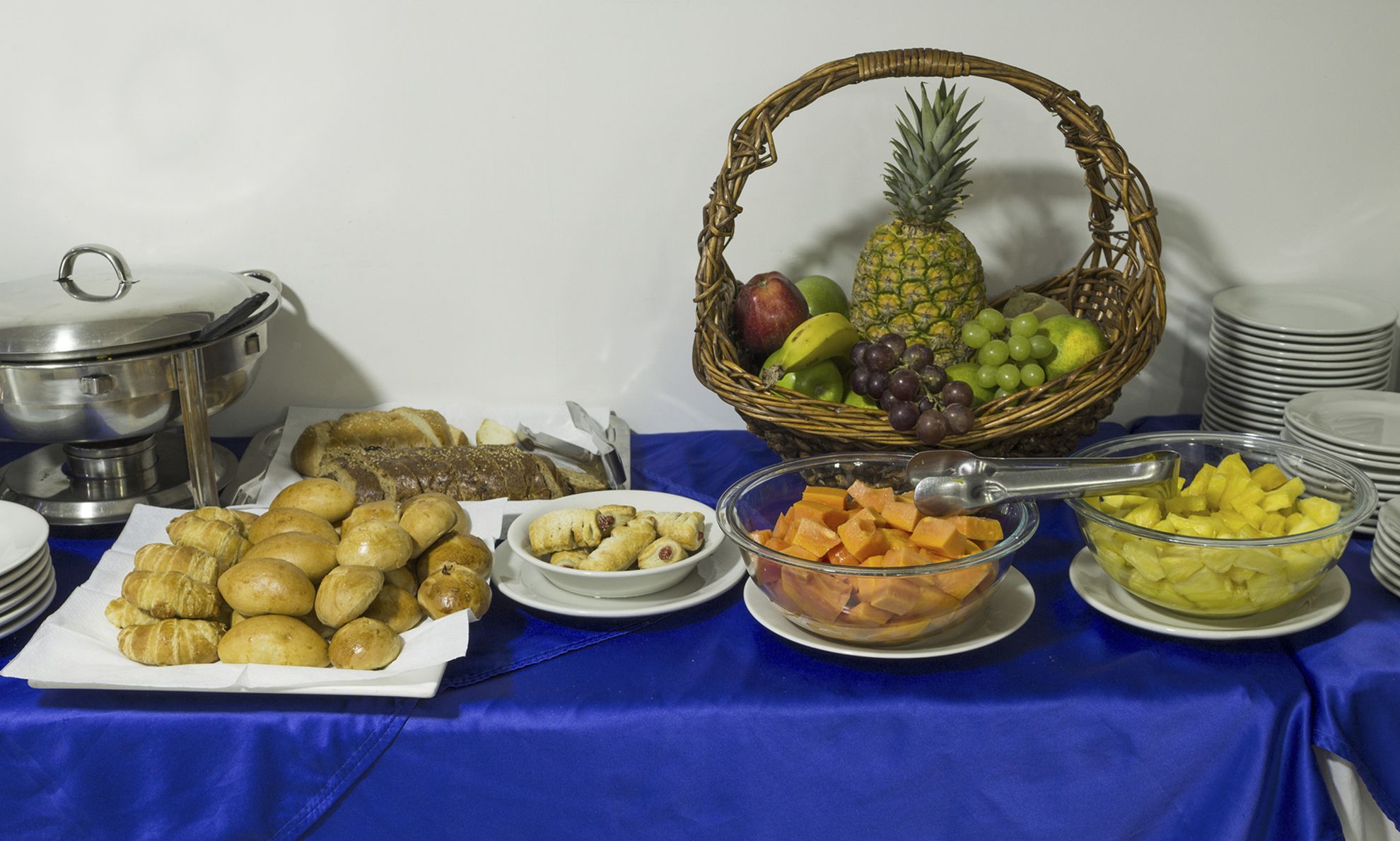 Una mesa de buffet con diversos alimentos, incluyendo pan, pasteles, frutas y una cesta de frutas.