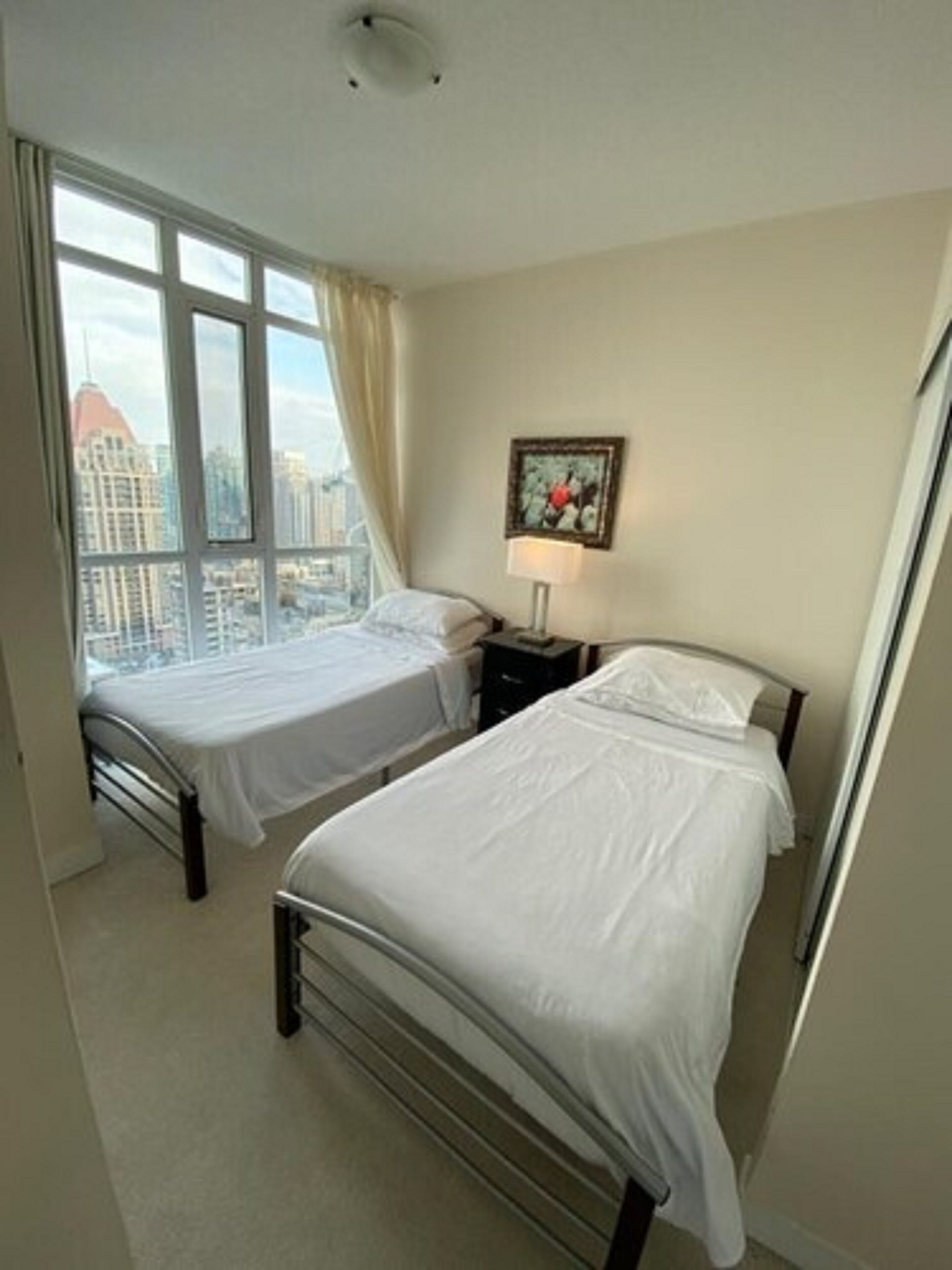 Habitación de hotel con dos camas, ventana con vista a la ciudad y un cuadro en la pared.