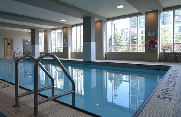 Piscina interna com água cristalina, corrimãos de metal e grandes janelas com vista para o exterior.