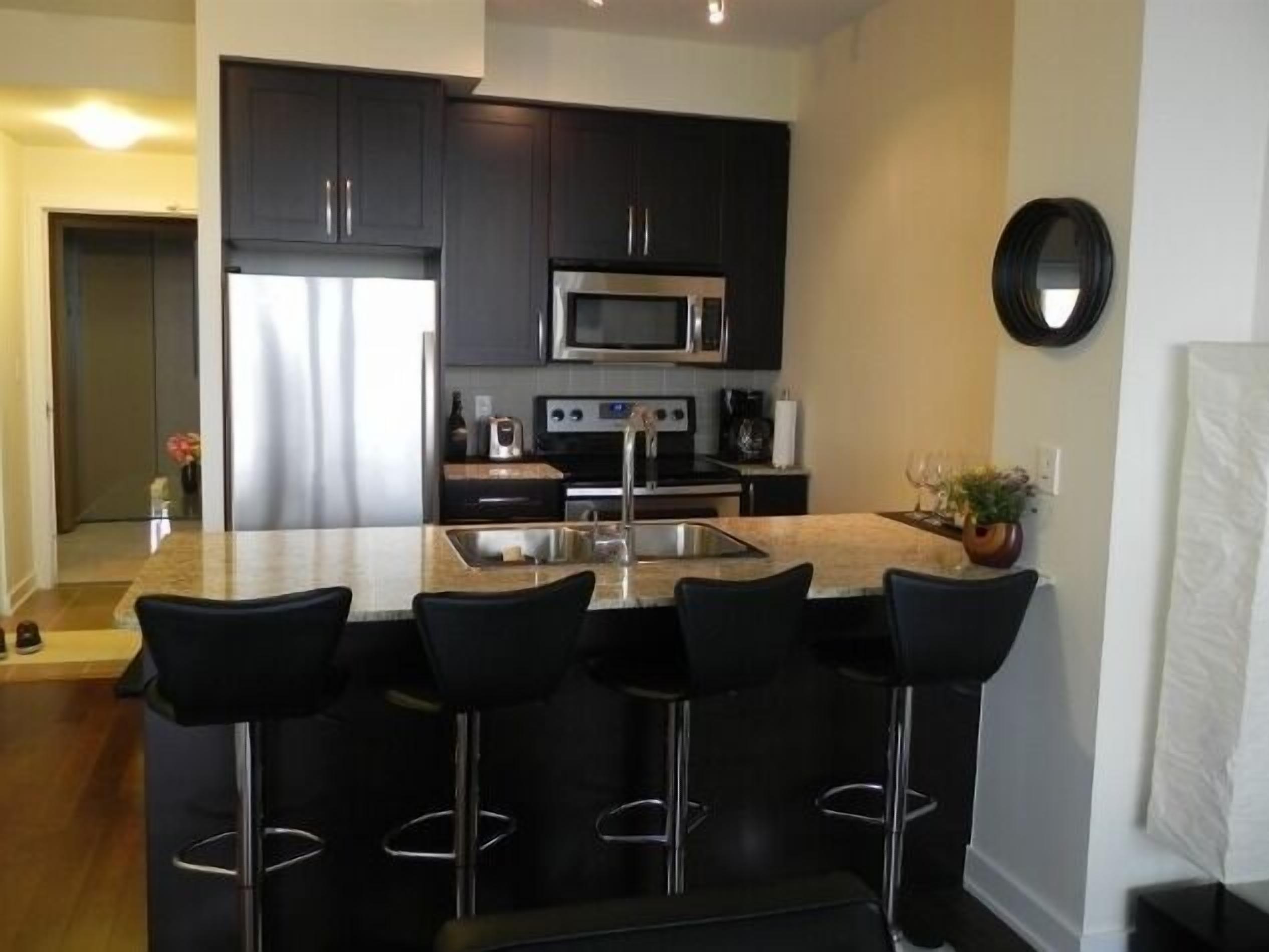 A modern kitchen with dark cabinets, stainless steel appliances, and a central island with bar stools.