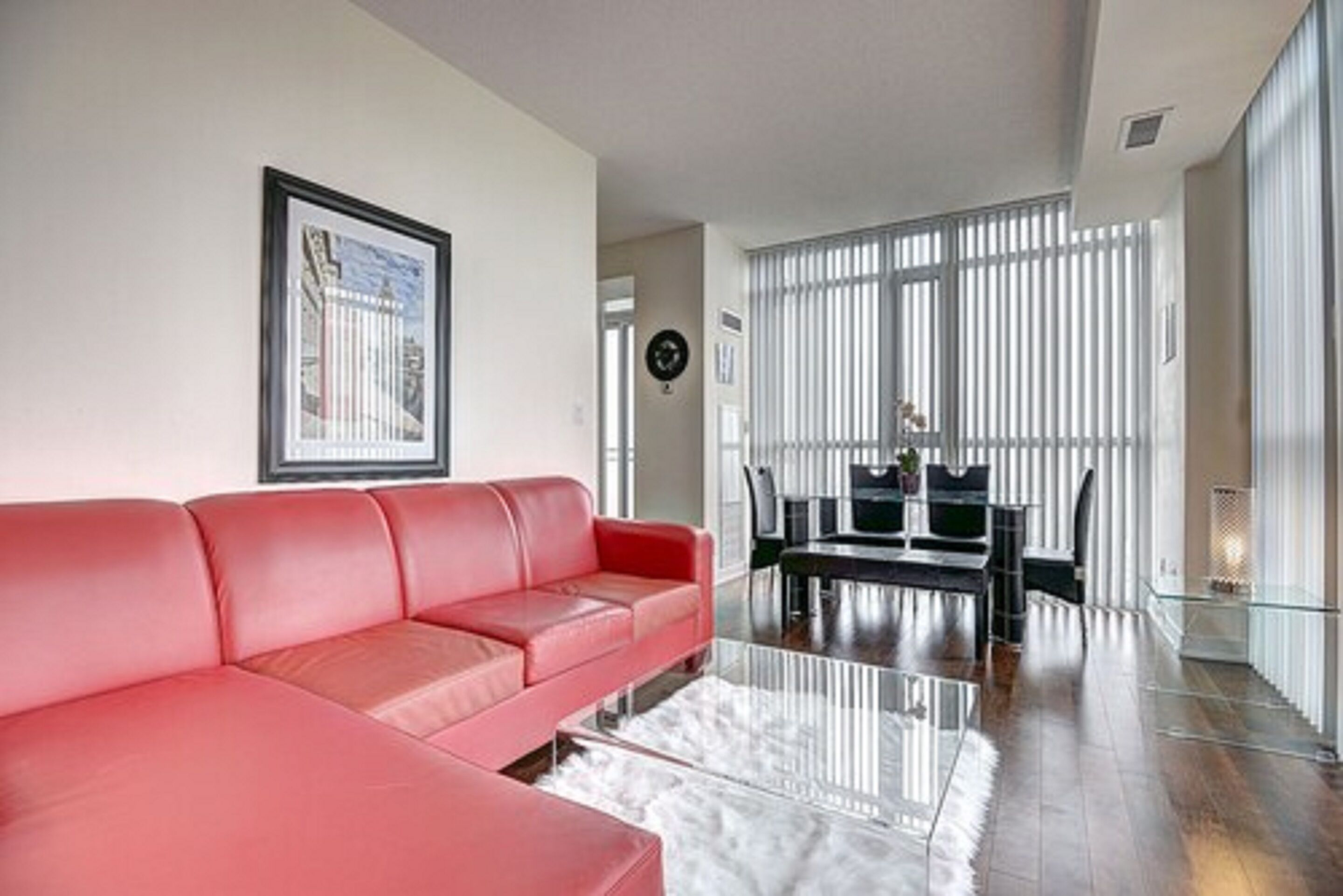 A modern living room with a red sofa, a glass coffee table, and a dining area with a black table and chairs.