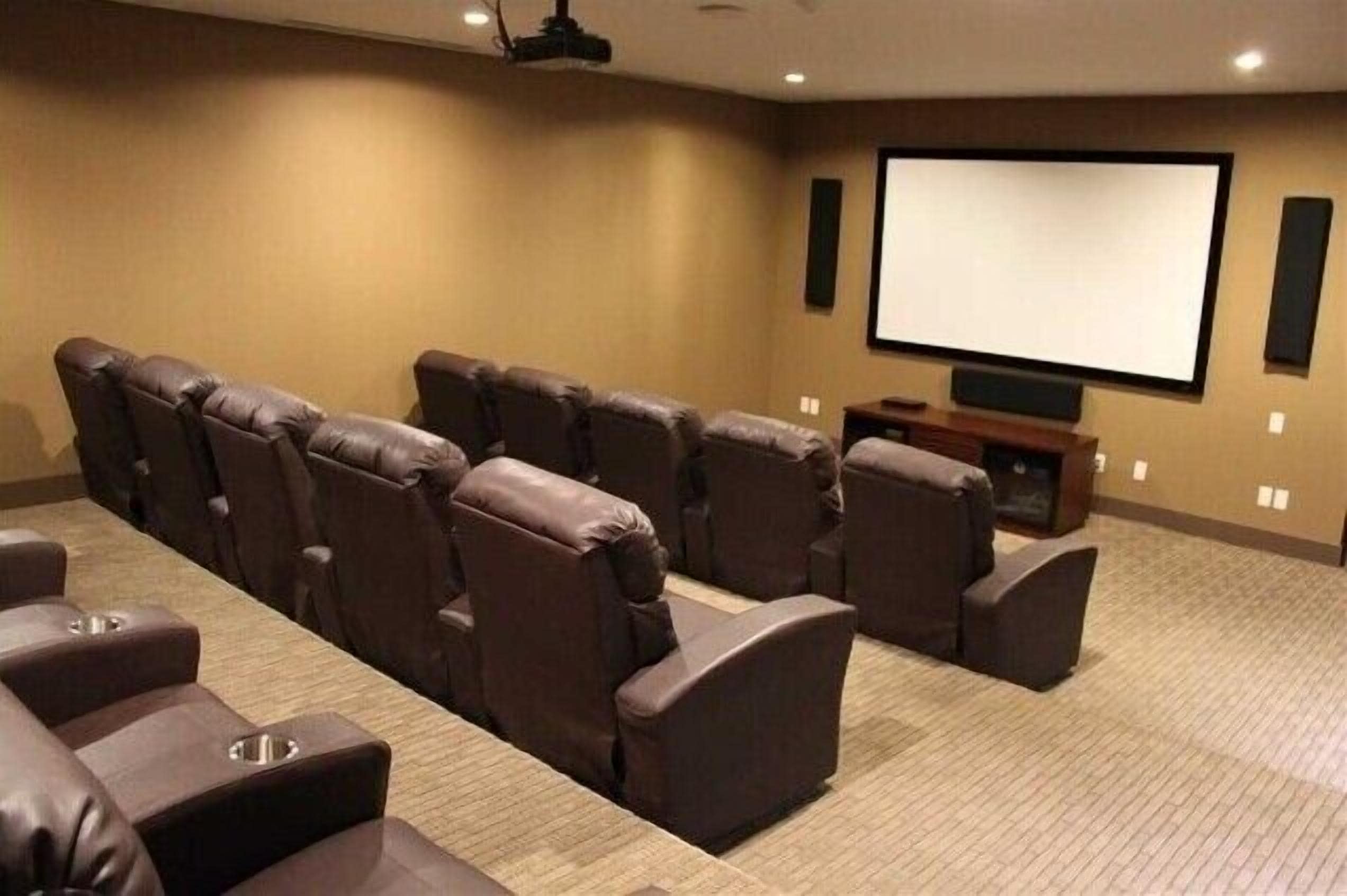 A home theater room with a large screen, reclining chairs, and a carpeted floor.