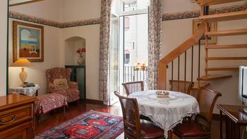 A dining area with a table set for two, surrounded by wooden chairs, a patterned rug, and a painting on the wall.