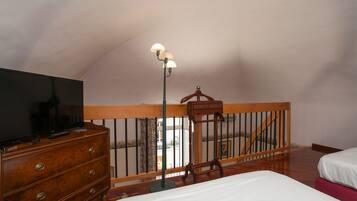 Quarto com cômoda de madeira, uma cama, mesa de cabeceira, abajur e guarda-corpo de varanda.