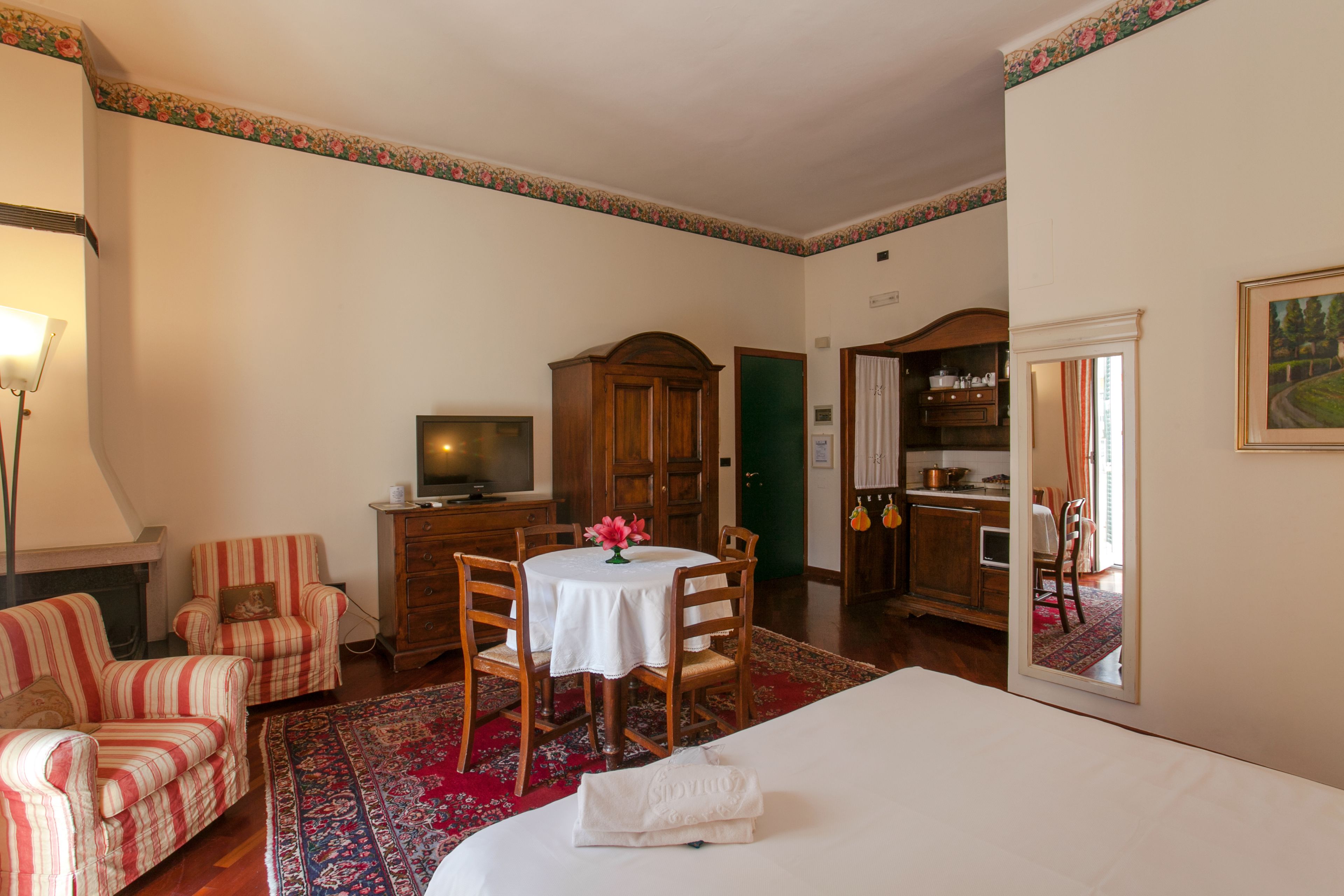 A hotel room with a bed, a dining table with chairs, a TV, a wooden cabinet, and a mirror.