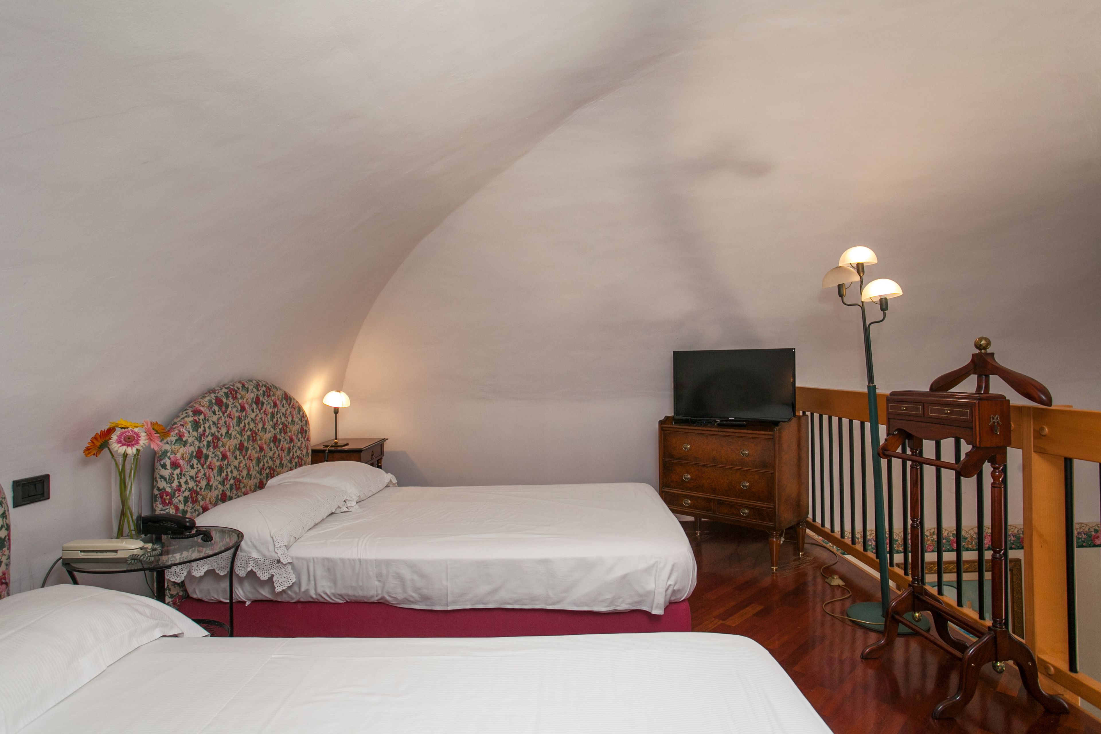 A bedroom with two beds, a wooden dresser, a television, and a lamp.