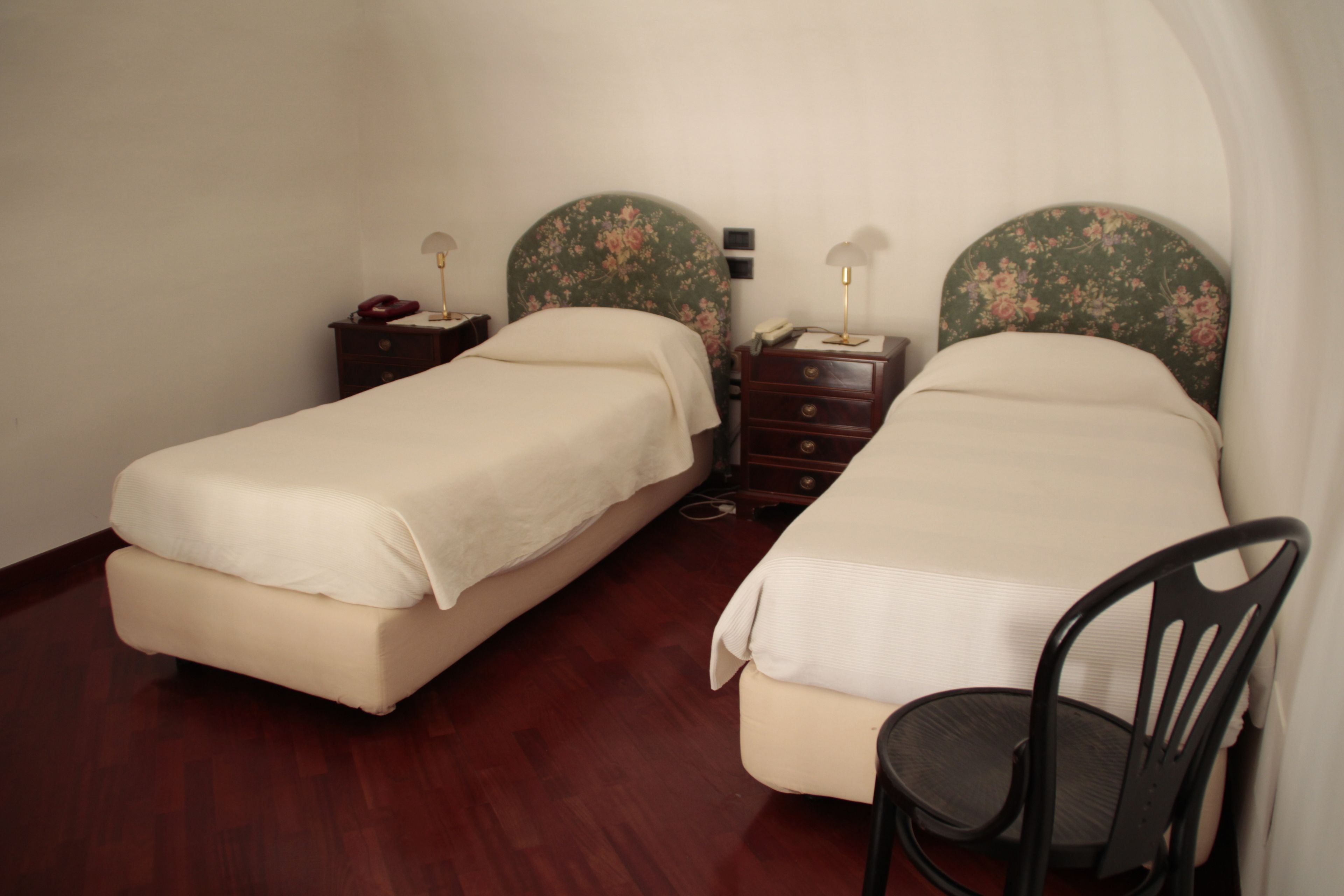 A room with two beds, a chair, a dresser, and a nightstand with a lamp.