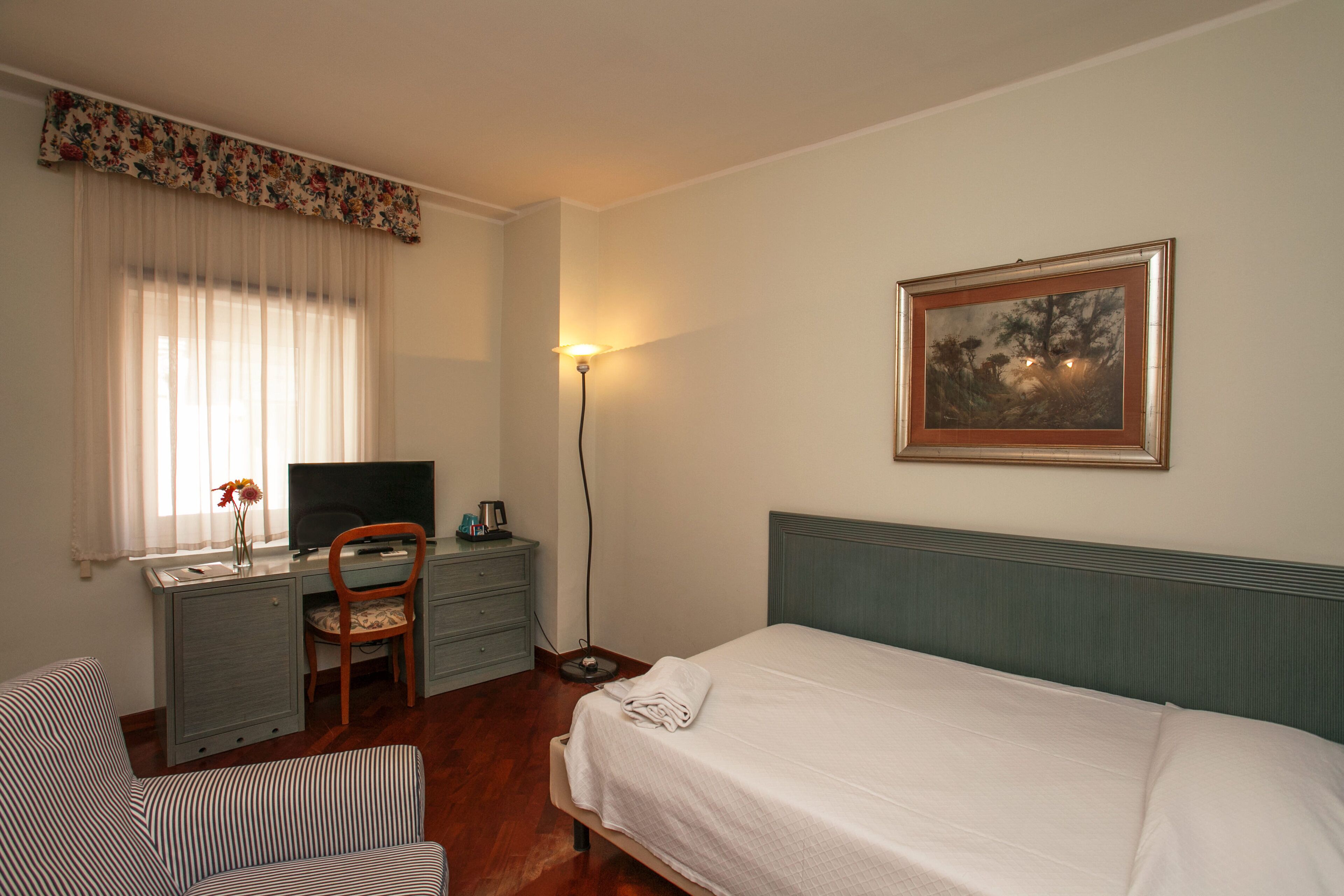 Una habitación de hotel con cama, escritorio, silla, televisor y un cuadro en la pared.