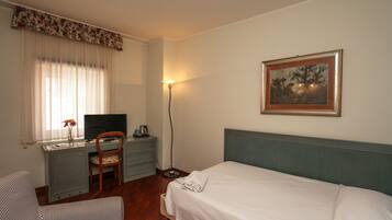 Una habitación de hotel con cama, escritorio, silla, televisor y un cuadro en la pared.