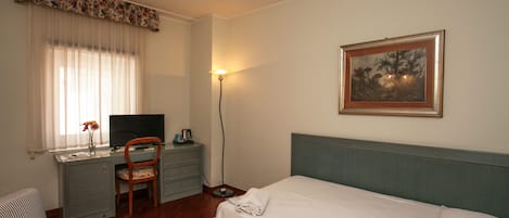 Una habitación de hotel con cama, escritorio, silla, televisor y un cuadro en la pared.