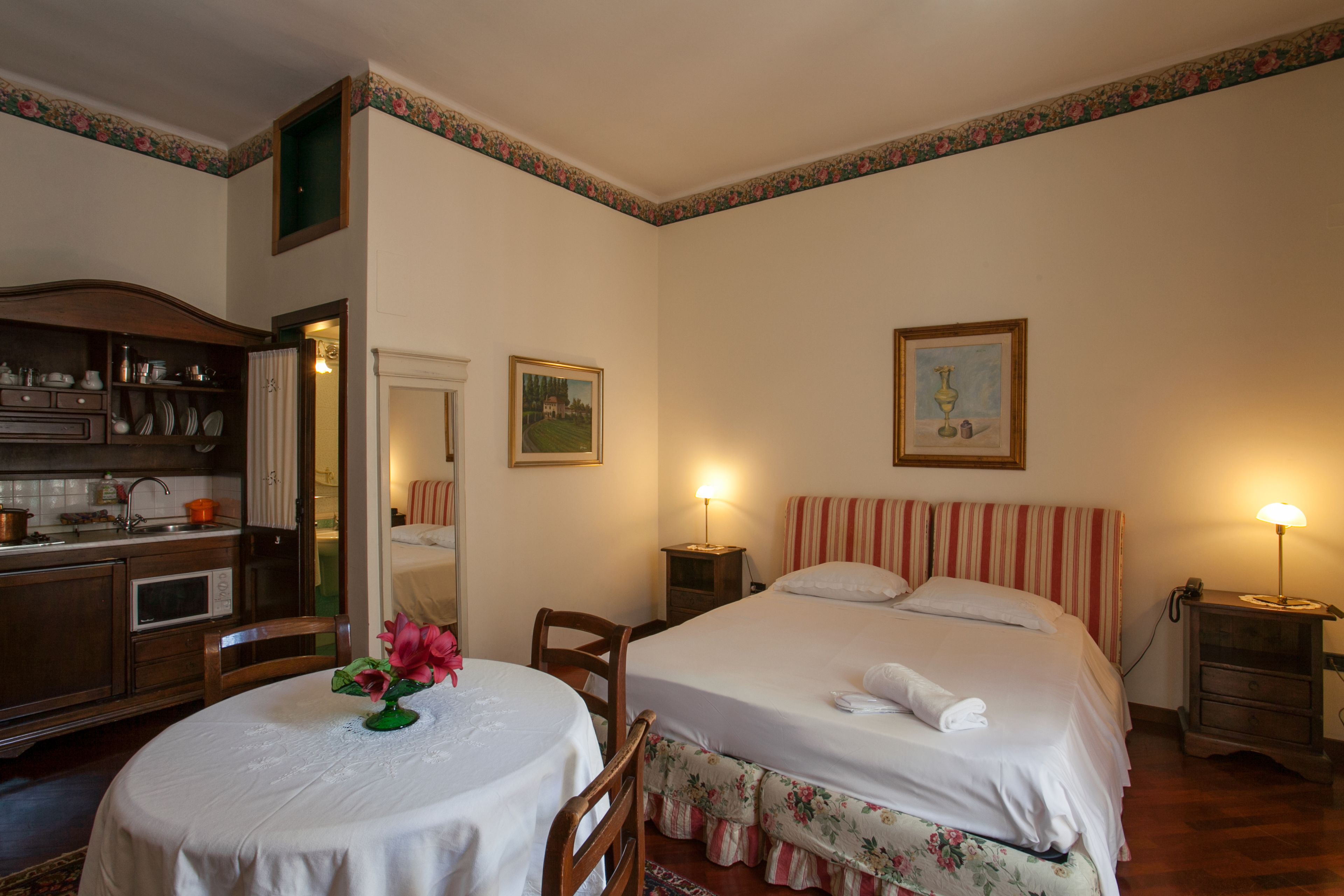 Une chambre d’hôtel avec un lit, une table de chevet, une lampe et une petite table sur laquelle est posé un vase de fleurs.