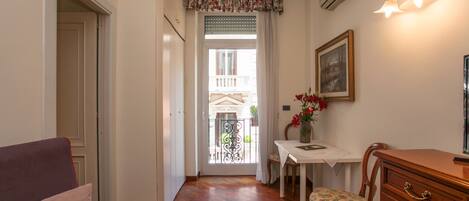 Un pasillo con piso de madera, una puerta, una silla, una mesa con un florero y un cuadro colgado en la pared.