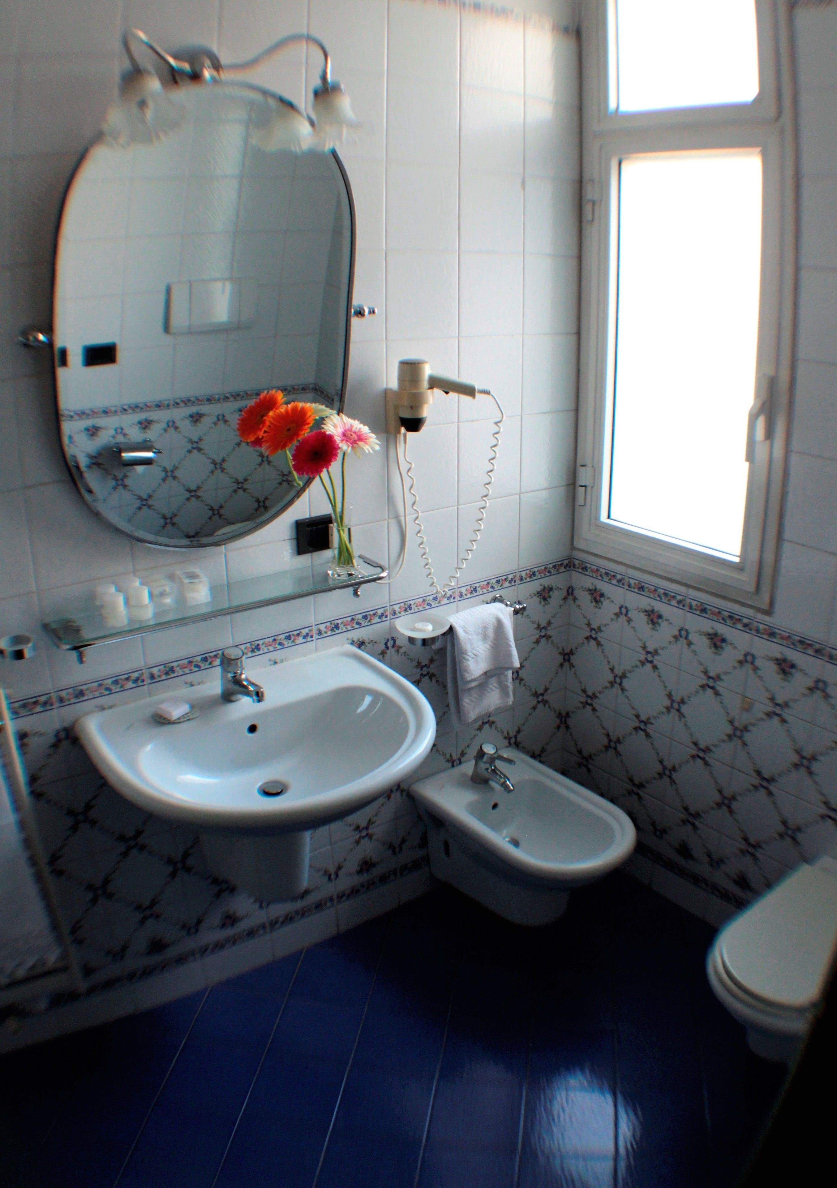 Un baño con lavabo, espejo e inodoro. Una ventana proporciona luz natural.
