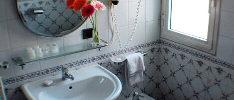 Een badkamer met een wastafel, spiegel en toilet. Een raam zorgt voor daglicht.