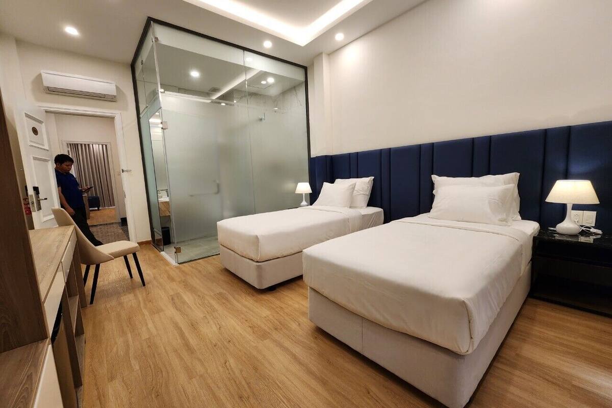A hotel room with two beds, a desk, a chair, and a glass partition.