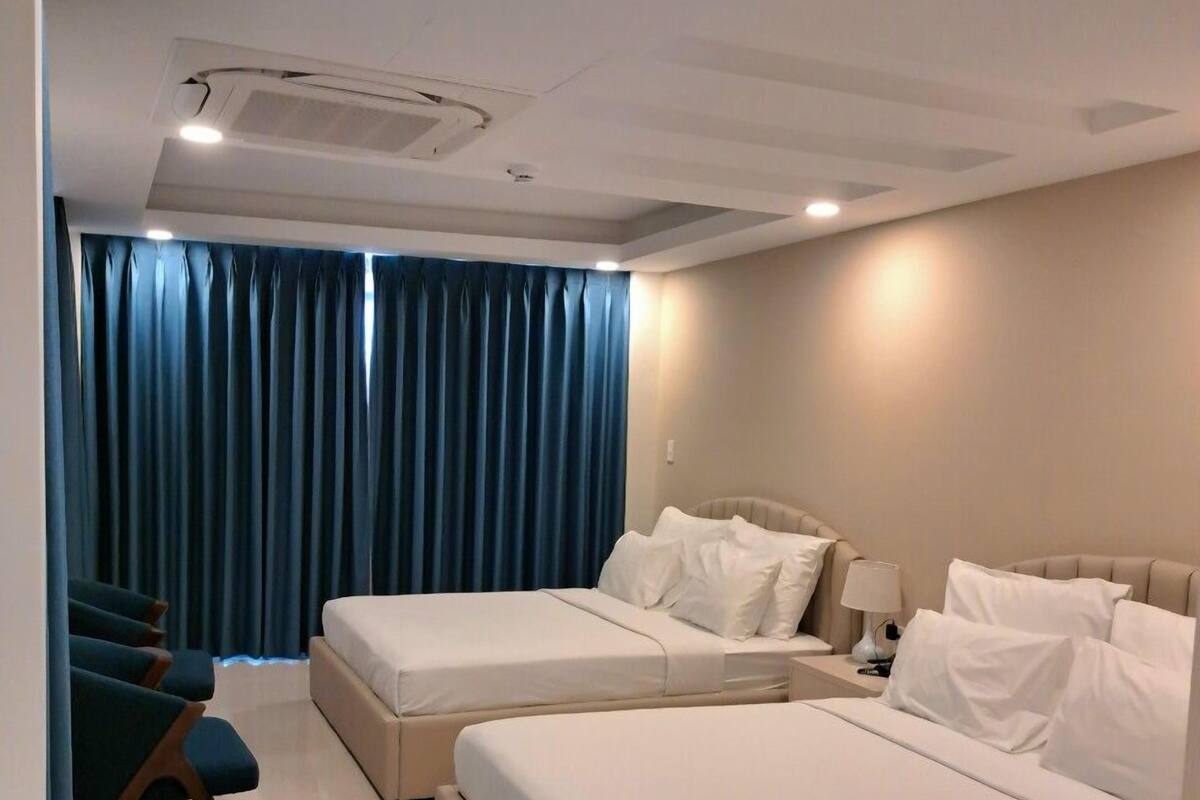 A hotel room with two beds, a desk, a chair, and a window with blue curtains.