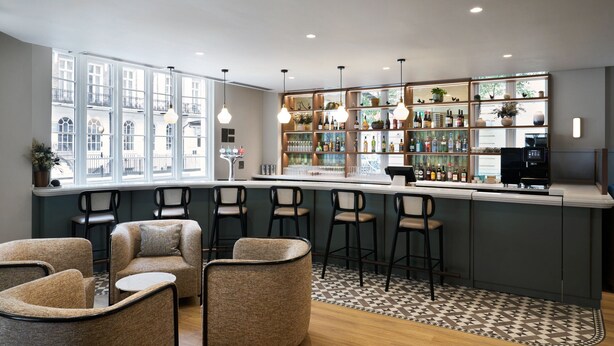 Un espace bar moderne, doté de sièges et d’un comptoir, offrant une vue dégagée grâce à de grandes fenêtres et agrémenté d’un tapis à motifs.