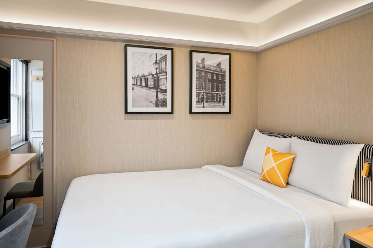 Une chambre d’hôtel avec un grand lit, un bureau et deux tableaux encadrés au mur.