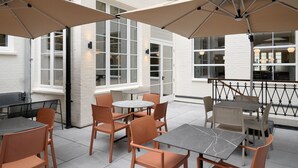 Un espace extérieur aménagé en terrasse, avec des tables rondes et des chaises orange, entouré de grands parasols.