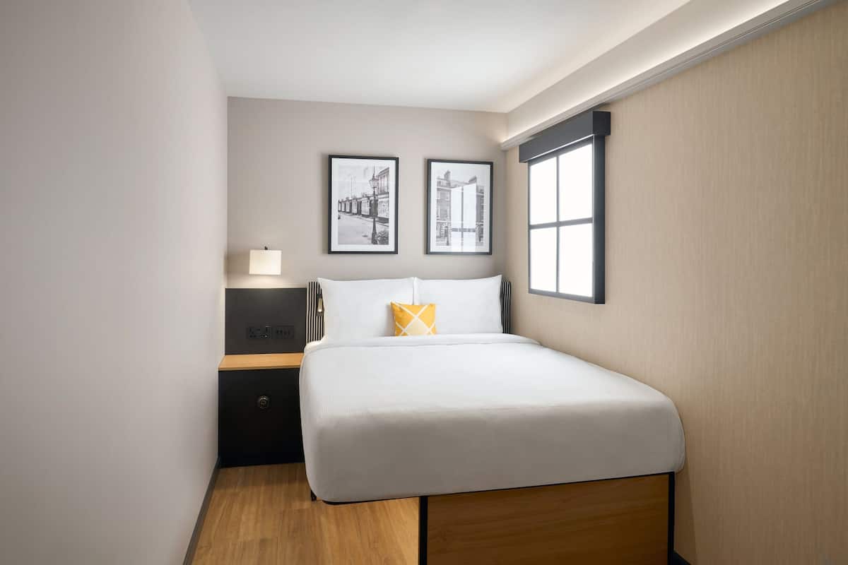 Une chambre bien rangée, avec un lit, une table de chevet, une lampe et deux tableaux encadrés accrochés au mur.