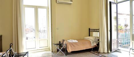 A hotel room with a bed, a chair, an air conditioning unit, and a view of the outside.