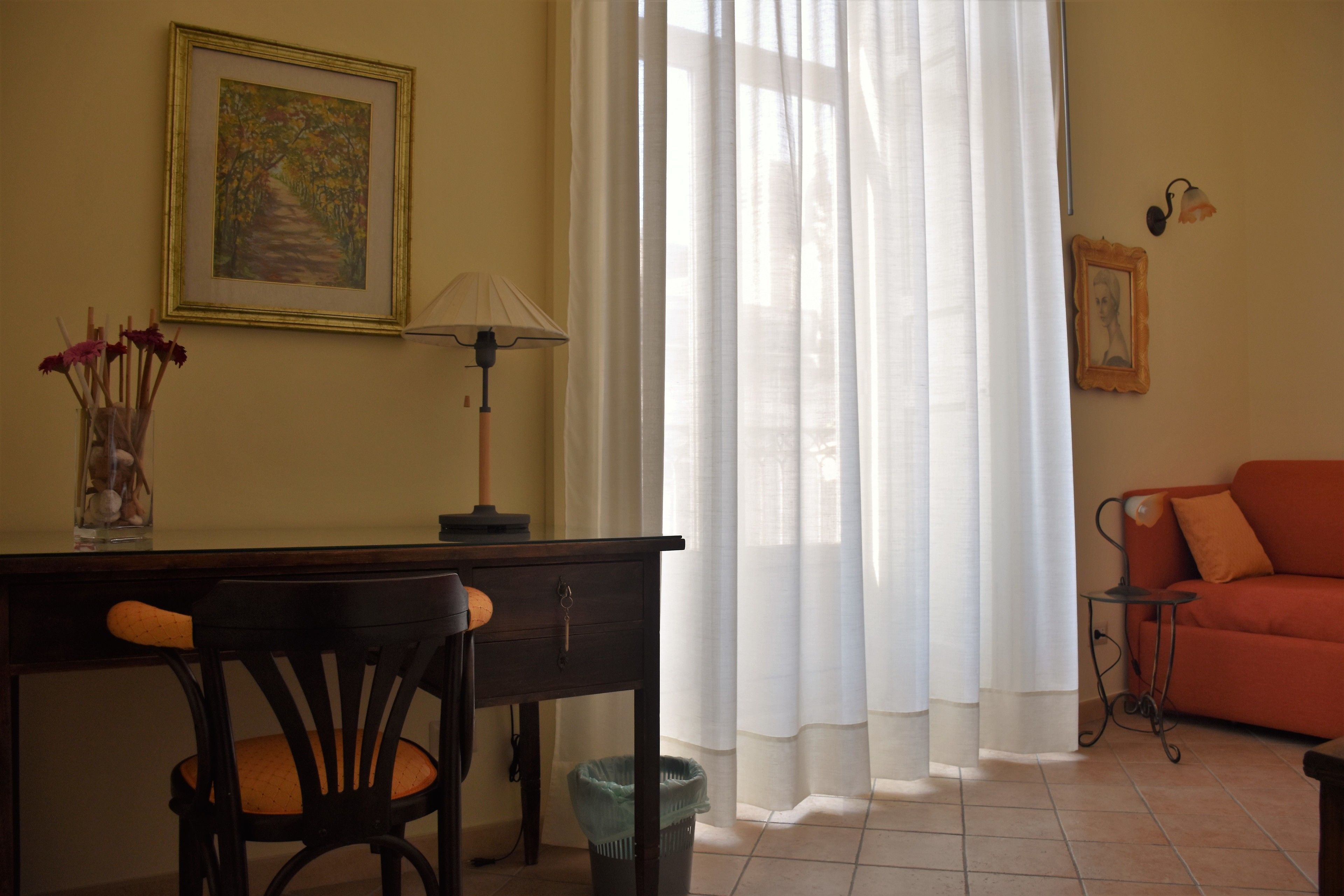 A room with a desk, chair, lamp, and a sofa.